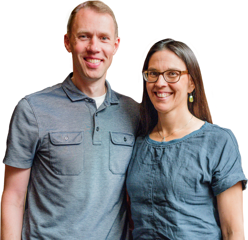 Portrait of Iain and Kalie Charnley standing together and smiling in front of a colorful geometric background.